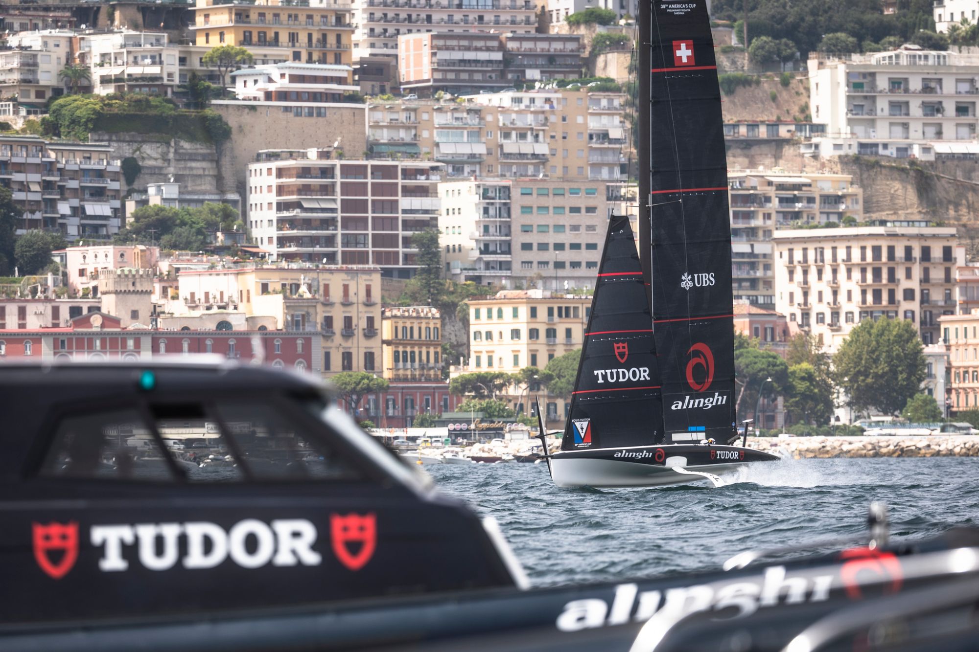 AC40 foiling yacht at speed with a chase boat in the foreground